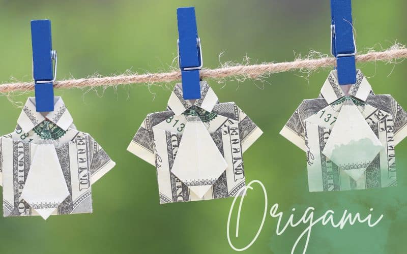 Hemden die aus Geldscheinen gefaltet sind an einer Leine mit kleinen blauen Klammern vor einem grünen Hintergrund.