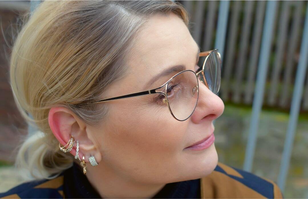 Eine Portraitaufnahme von der Seite. Eine blonde Frau trägt ein filigranes Brillengestell in Gold und Schwarz,