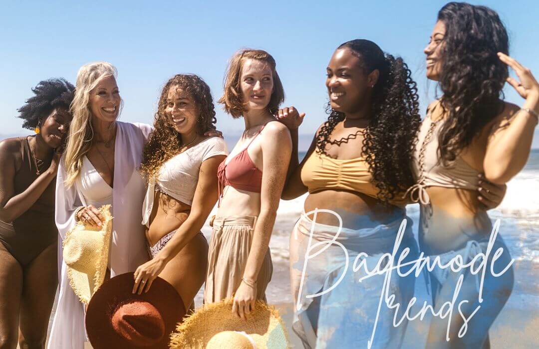 Sechs Frauen mit unterschiedlichen Hautfarben und Körperformen stehen in Badeanzügen und Bikinis vor einem sommerlich blauem Himmel.