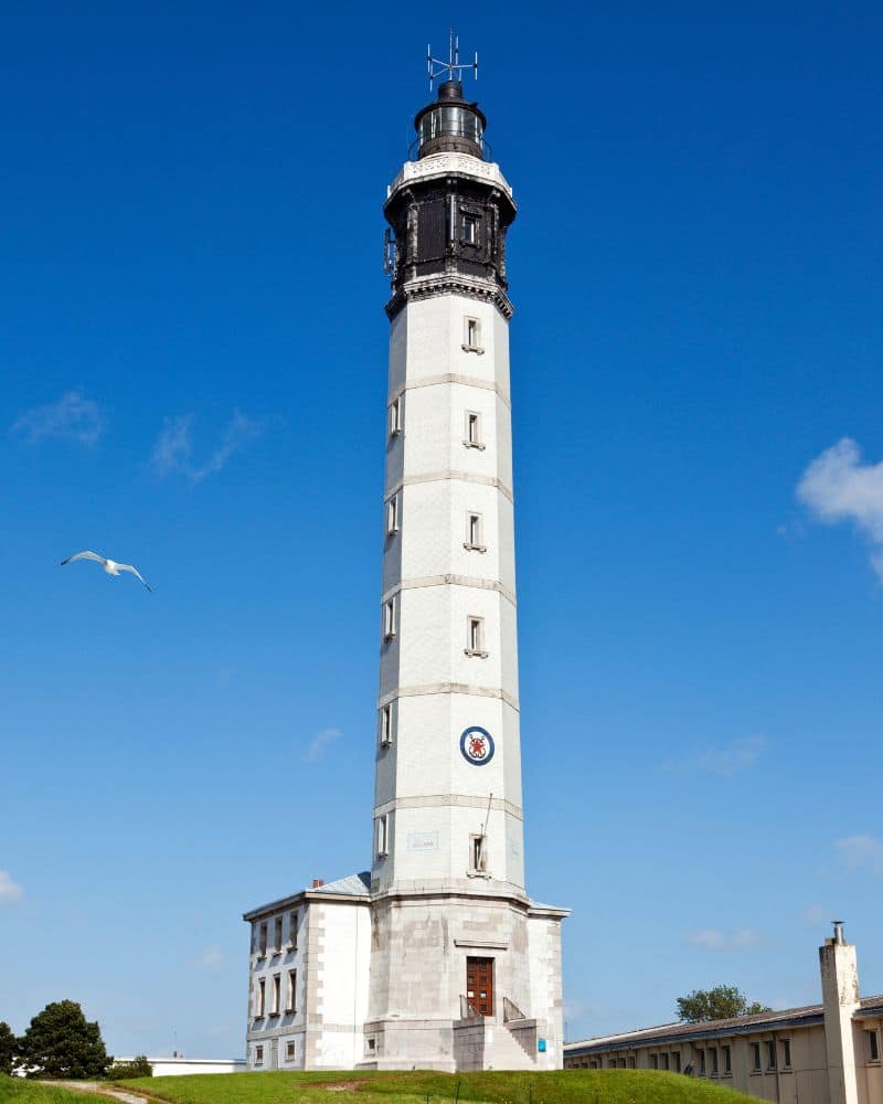Der hohe, weiße Leuchtturm von Calais erstreckt sich in den blauen Himmel.