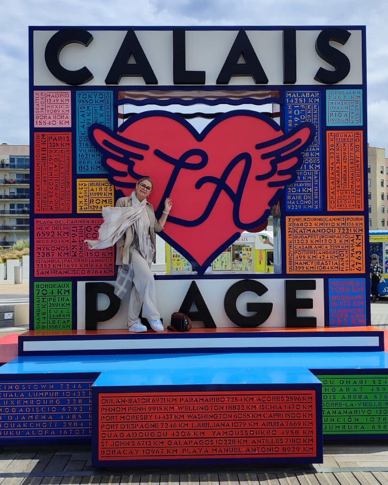 Das bunte Stadtzeichen von Calais mit einer Frau die davor steht.