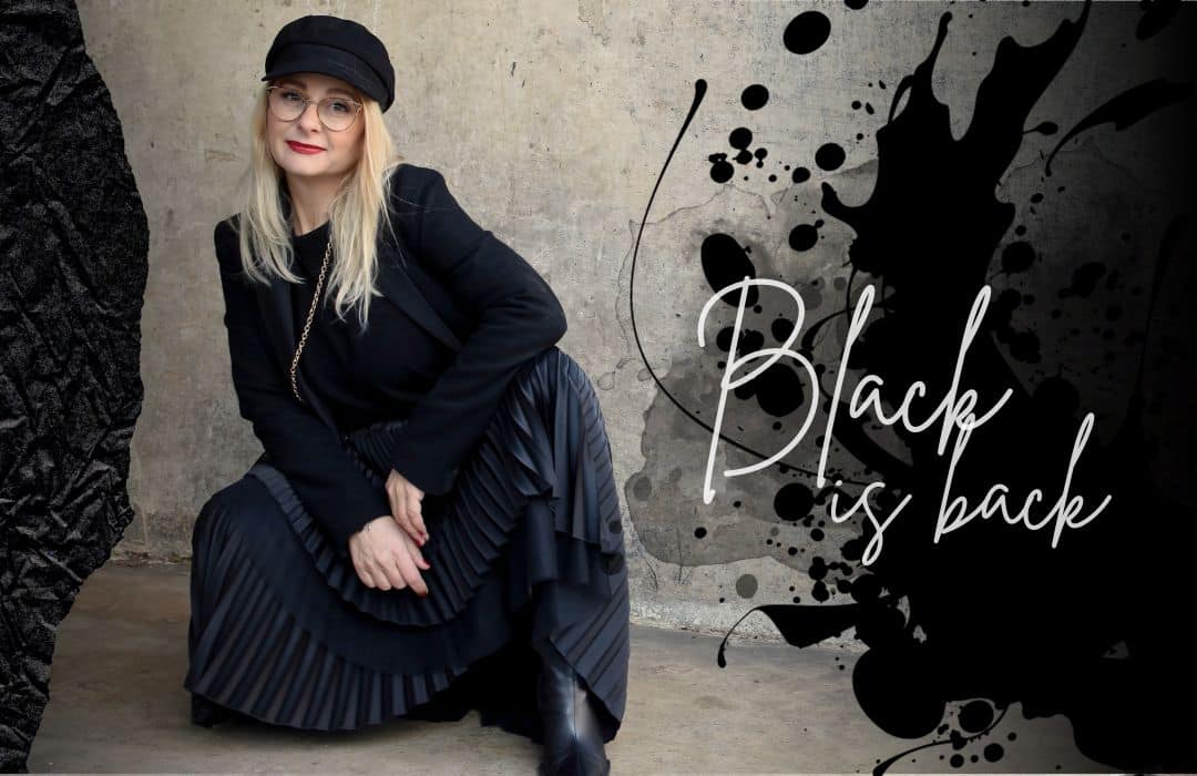 Frau mit Outfit komplett in Schwarz sitzt vor einer Wand.