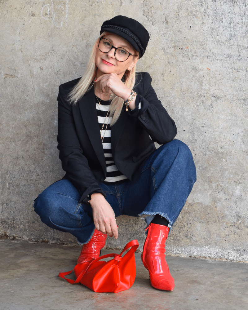 Stylischer Look mit Barrel Jeans: Schwarz-weißes Streifenshirt, Blazer, Fiddler Cap und rote Highlights als modischer Eyecatcher.
