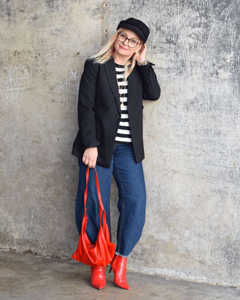 Stylischer Look mit Barrel Jeans: Schwarz-weißes Streifenshirt, Blazer, Fiddler Cap und rote Highlights als modischer Eyecatcher.
