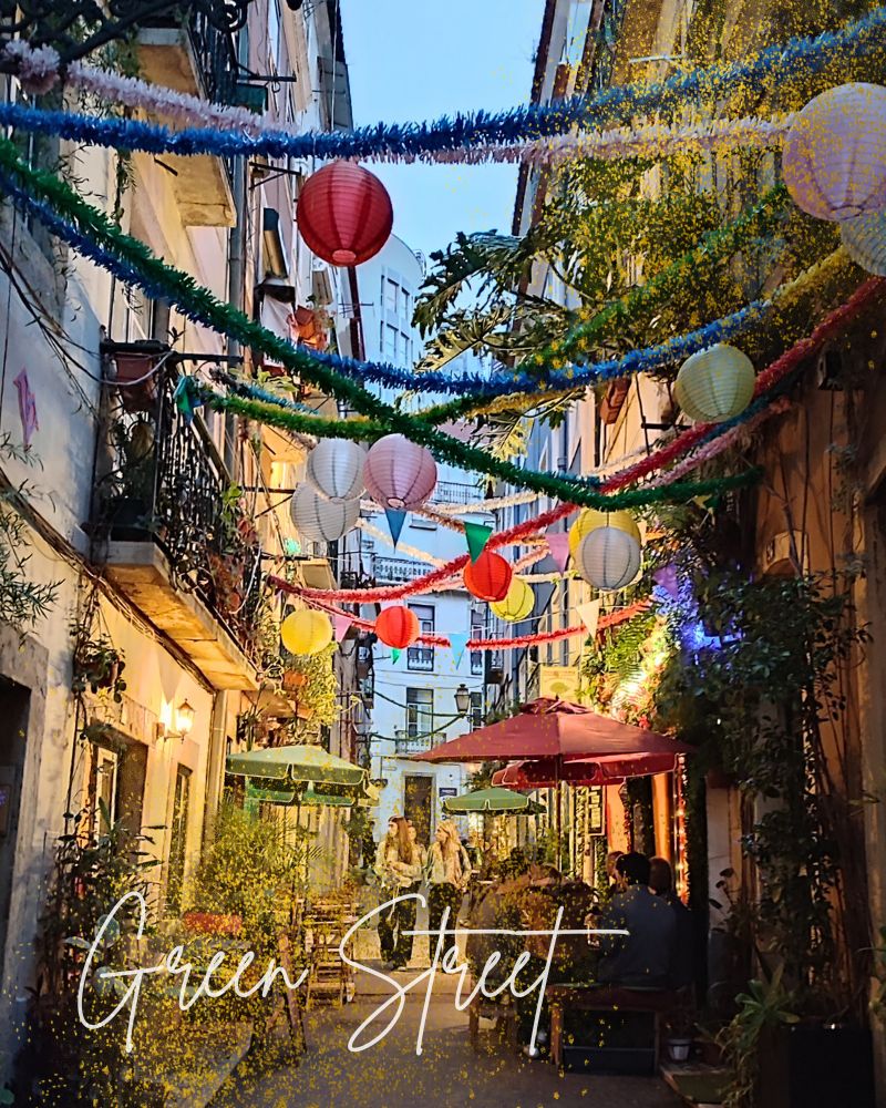 Abendlicher Blick in die Green Street in Lissabon. Menschen sitzen in Cafes und bunte Girlanden und Lampinons erleuchten die Häuser.