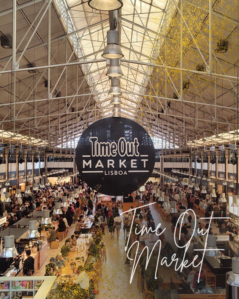 Blick in die Markthalle des Time-Out Markets in Lissabon. Menschen sitzen an Tischen und essen unter der dreieckigen Stahlkonstruktion des Daches.