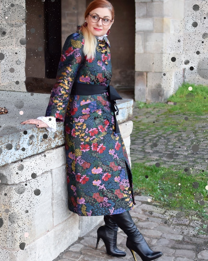 Frau trägt Herbst Trend Dark Romance Outfit mit dunklem Mantel mit Blumenprint und Rüschen