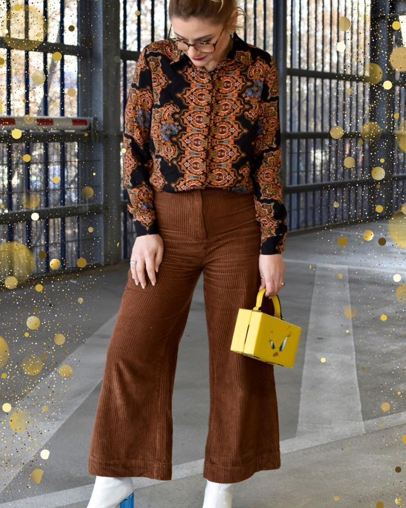 Eine Frau trägt eine braune Hose in Breitcord und dazu eine gemusterte Bluse.